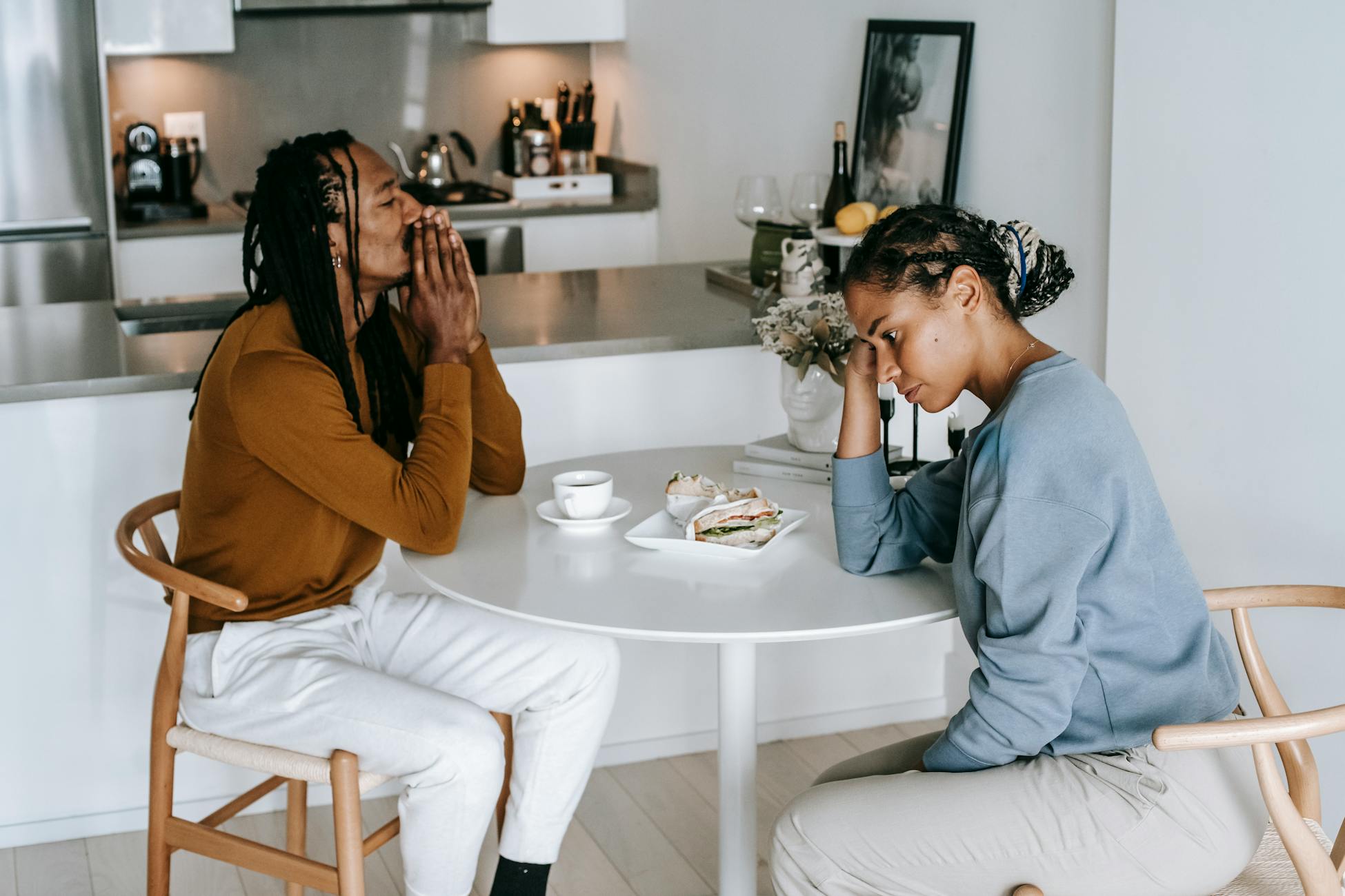 Young African American man sitting at table with woman and looking down thoughtfully while having conflict