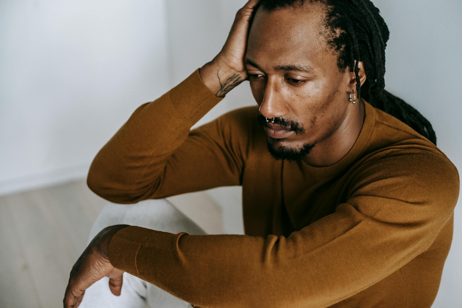 A contemplative man with dreadlocks sits indoors, expressing introspection and solitude.