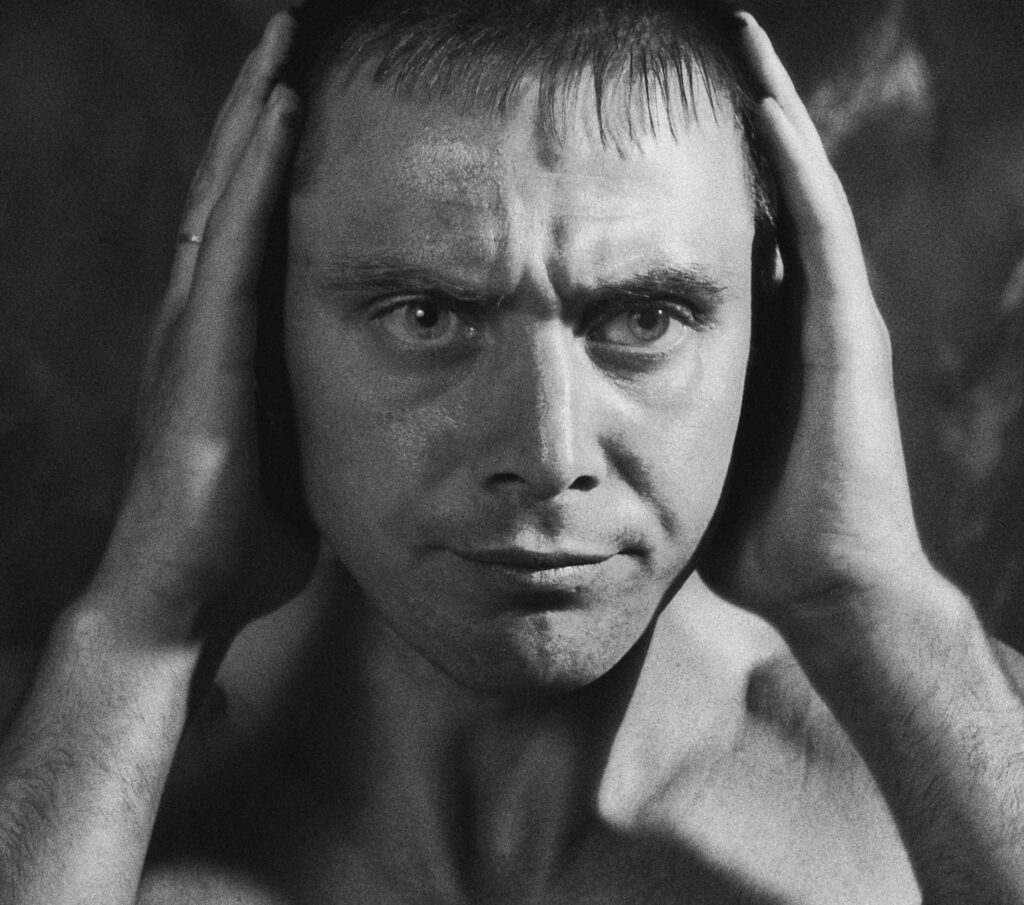 Close-up grayscale portrait of a serious man with hands to head, highlighting emotional intensity.