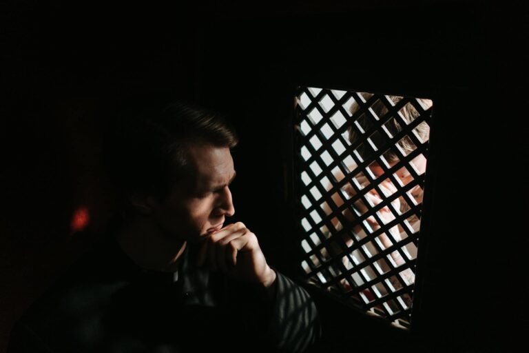 A solemn scene captures a man in deep thought during a confession session inside a dimly lit church.
