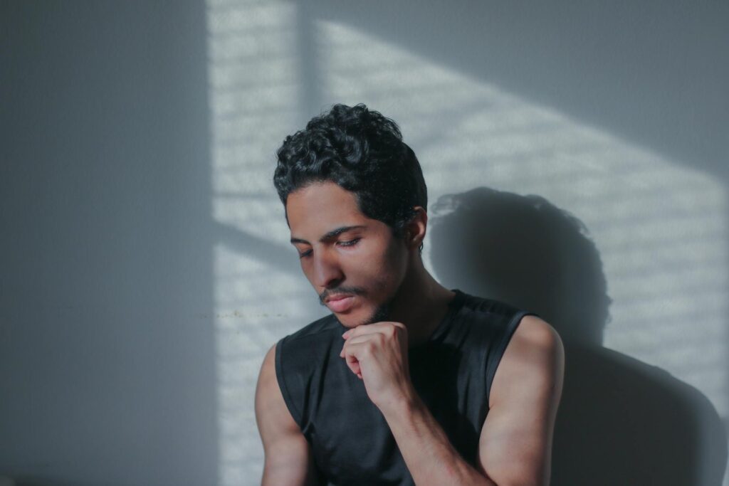 A man with a thoughtful pose, highlighted by striking shadows on a wall.