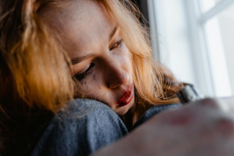 Close-up of a woman with red hair in a thoughtful and emotional moment indoors.