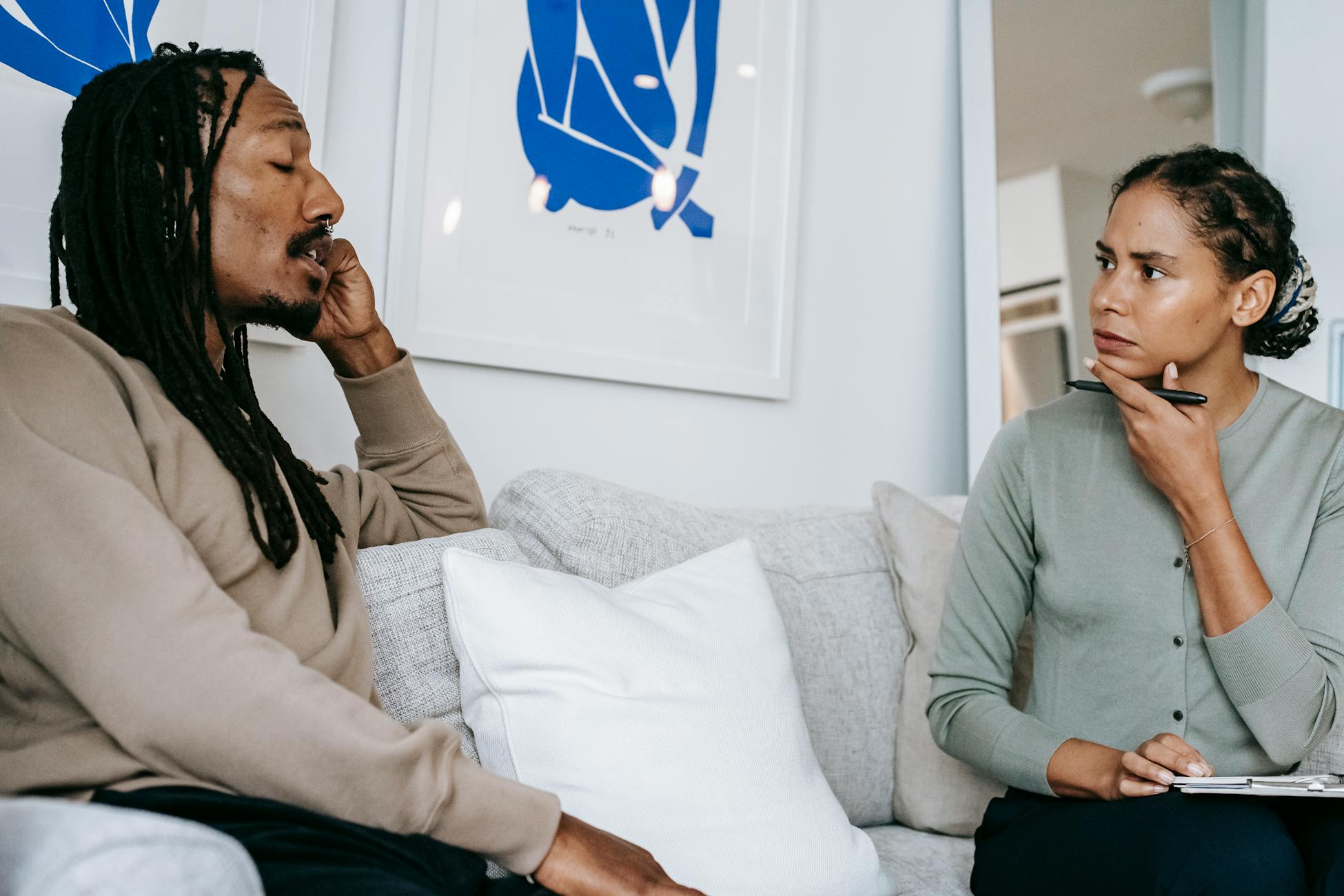 Attentive ethnic female stressed in formal wear sitting on sofa and listening to Concerned African American male client in modern psychology center