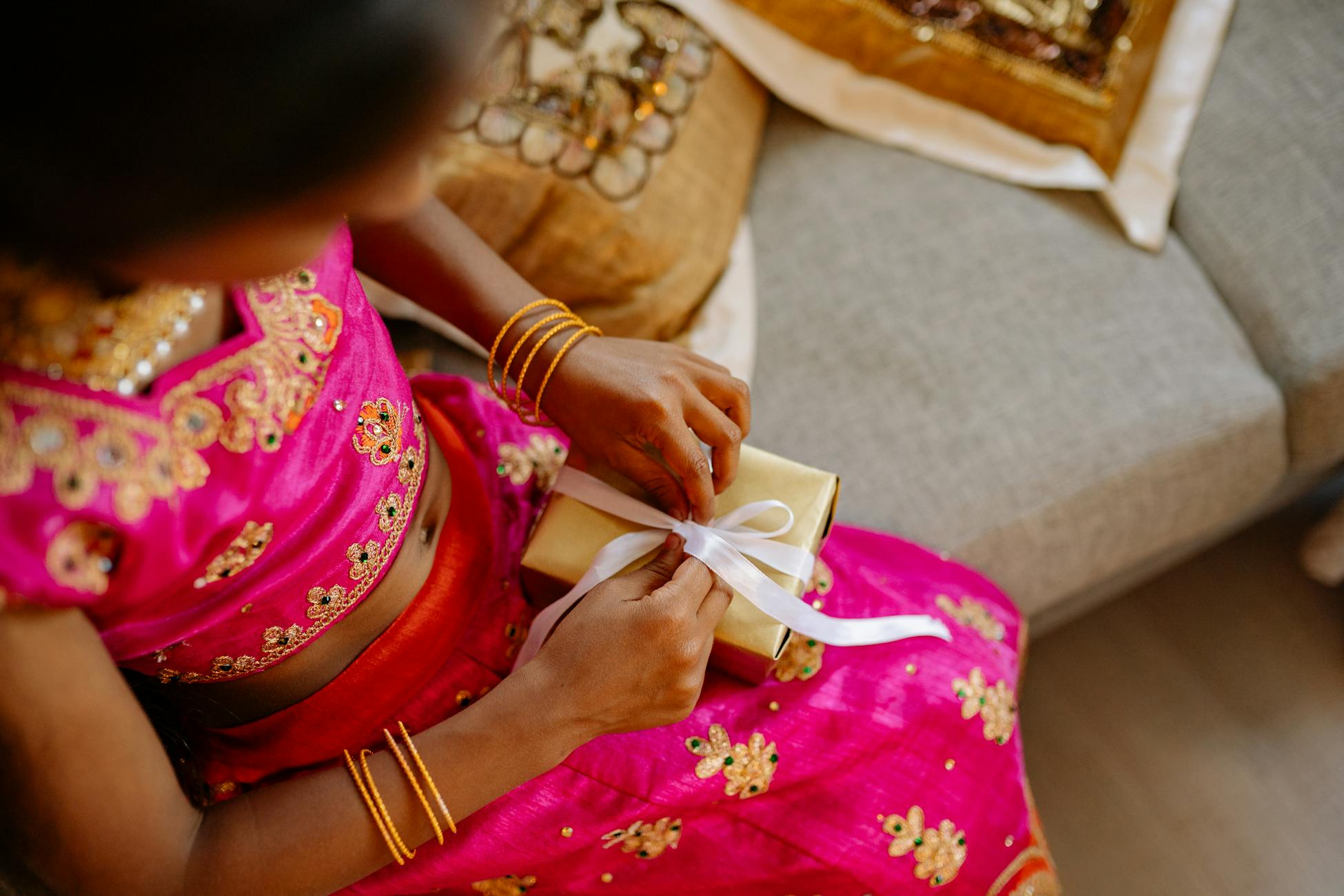 An Indian woman in traditional attire holding a Diwali gift indoors, symbolizing culture and celebration.