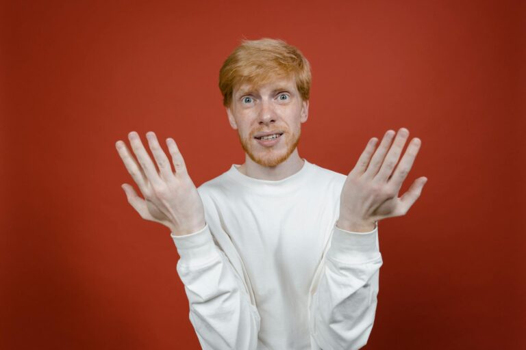 Caucasian man with ginger hair and beard gesturing against a red background in a studio portrait.