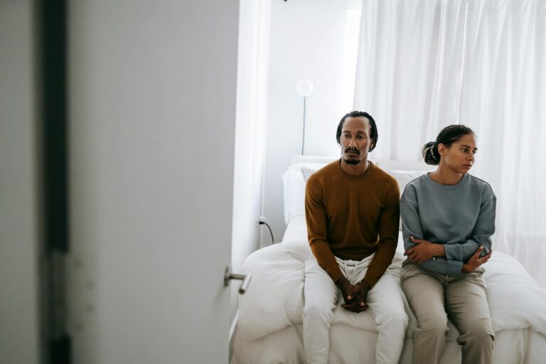 Young African American couple in casual outfit sitting on bed together with sad face in daytime