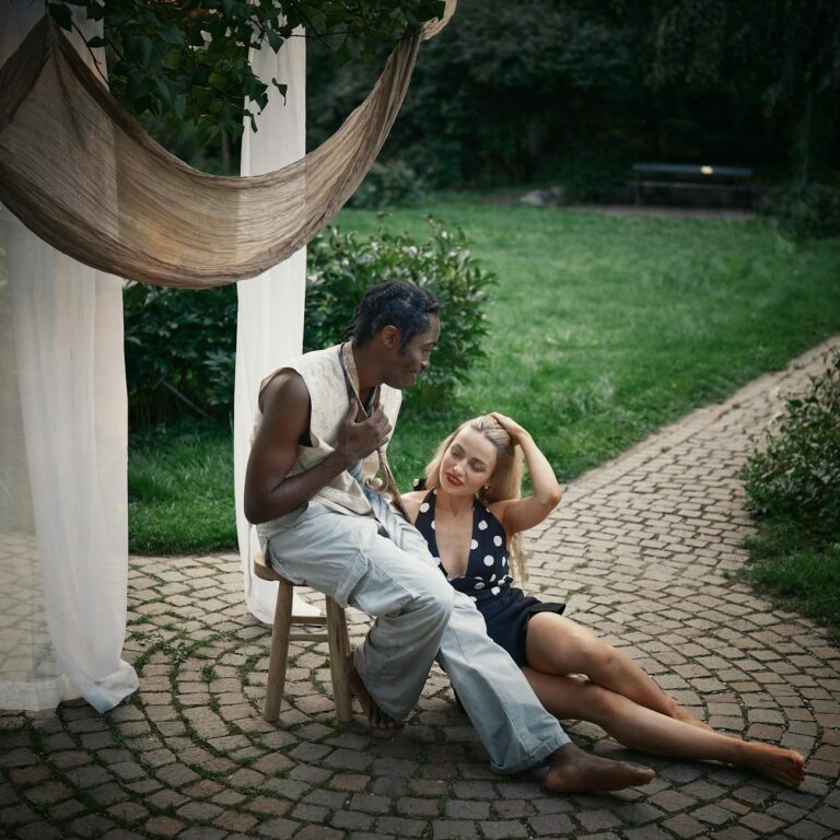 A couple enjoys a peaceful moment together in a lush garden setting, seated on cobblestone.