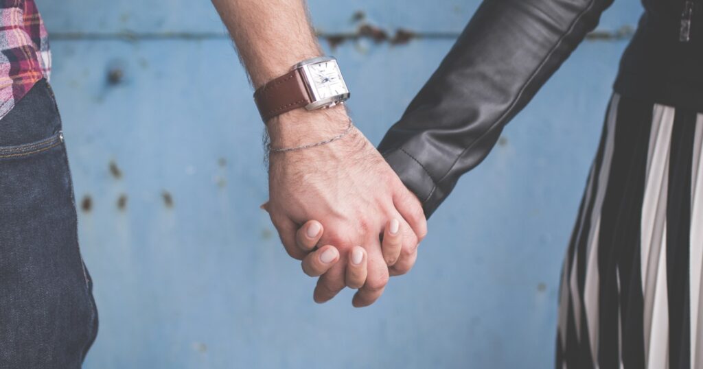 Two people holding hands in front of a pale blue wall