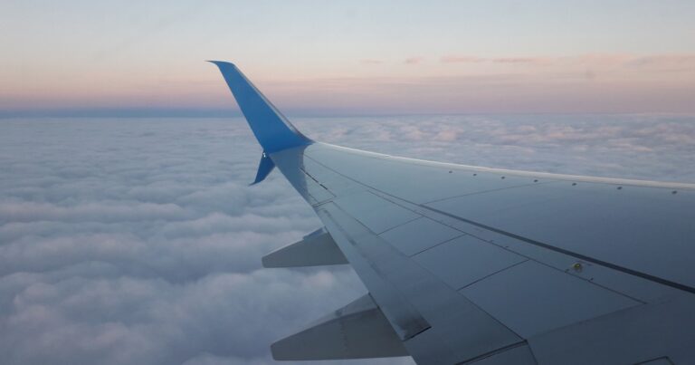 Airplane wing over a soft sea of clouds with a warm dawn horizon