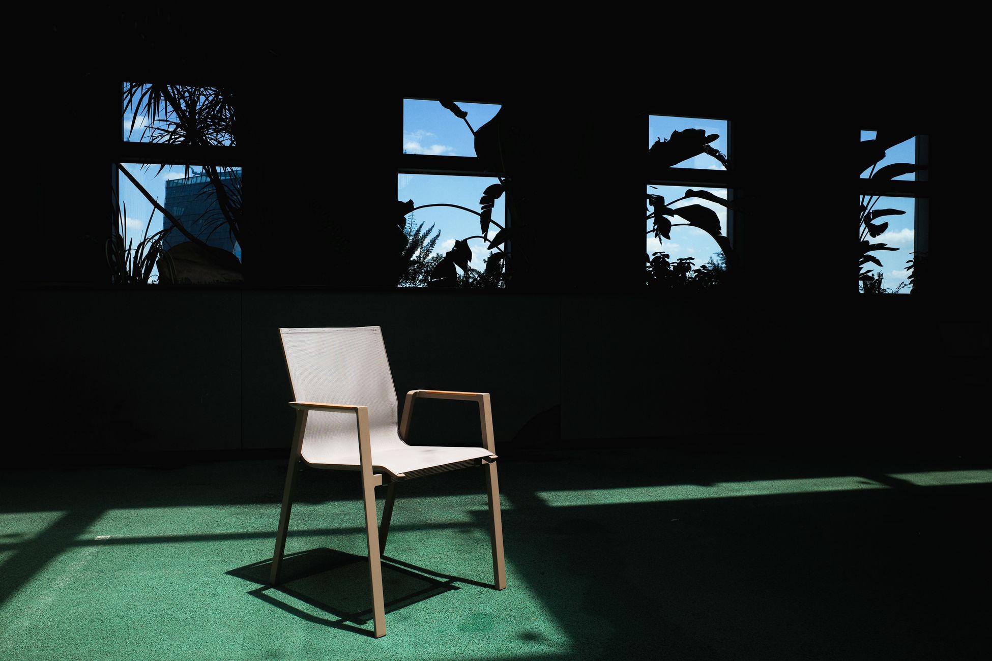 Minimalist chair in shadowy room with lush outdoor view through windows.