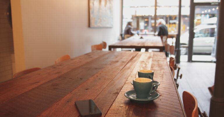 Two espresso cups and a phone resting on a wooden cafe table in warm window light