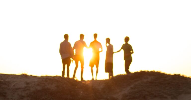 Five people stand together in silhouette on a dune ridge, the low sun setting behind them.