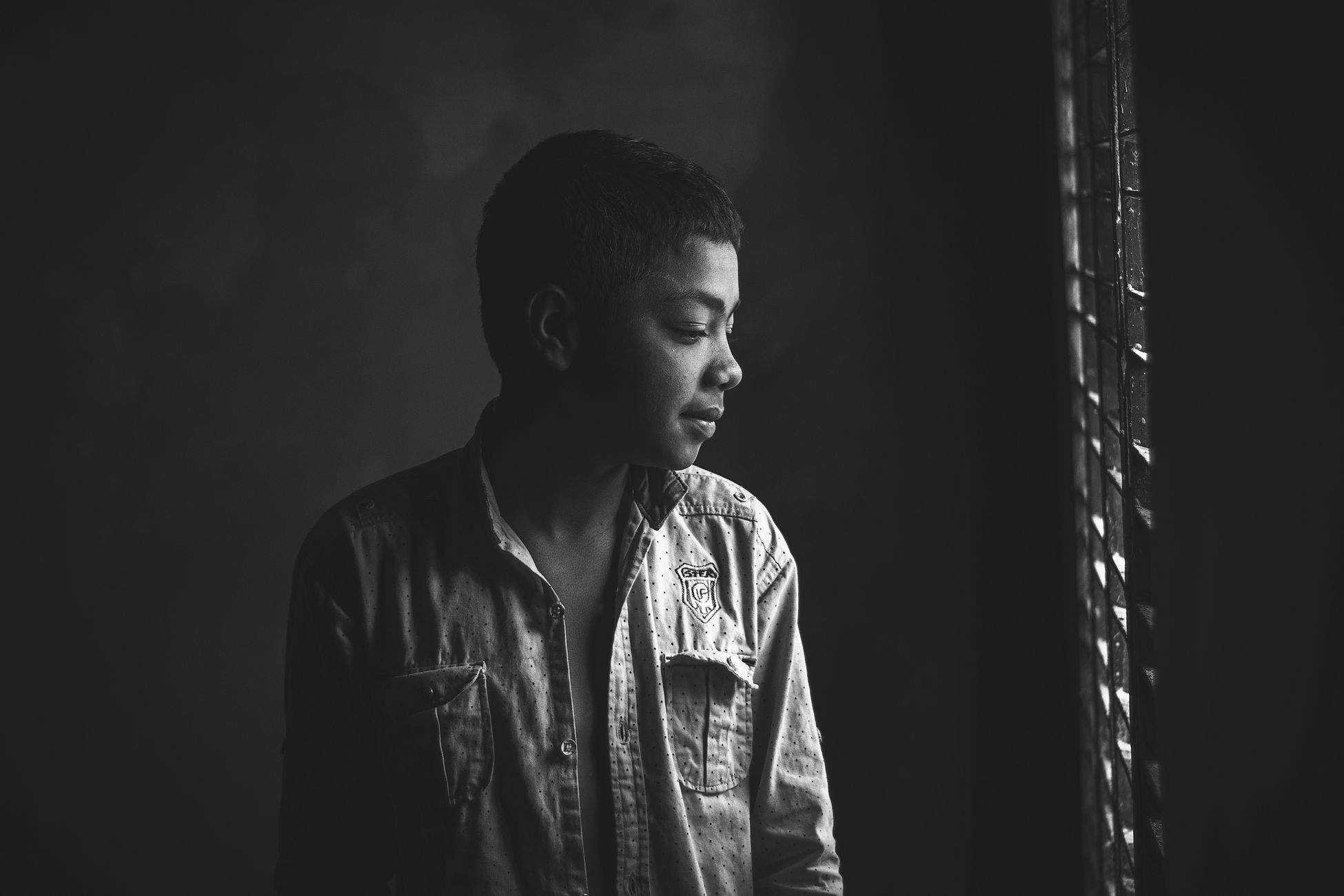 Monochrome portrait of a young boy looking out a window, lost in thought.