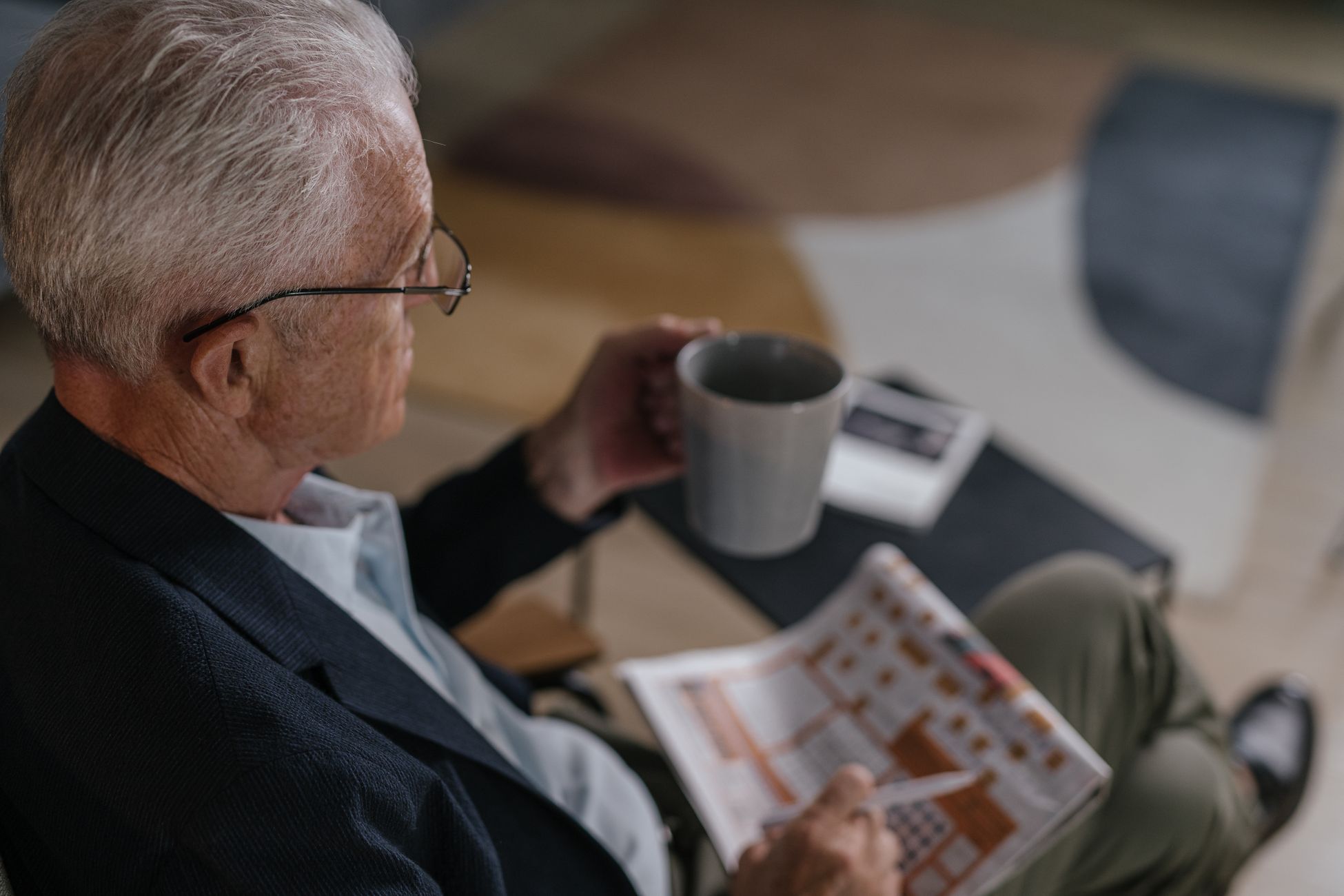 Senior man enjoying coffee while reading a newspaper indoors, exuding calm and relaxation.