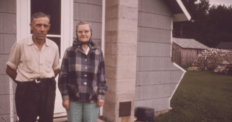 An older couple standing side by side outside their farmhouse, photographed in the 1970s