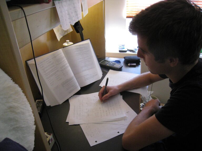 Young adult studying at a desk with textbook, notes, and calculator
