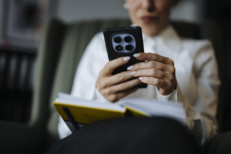 Close-up of adult hands holding a smartphone over an open notebook