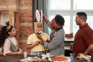 Family gathering with kids creating Easter bunny mask indoors, enjoying seasonal food.